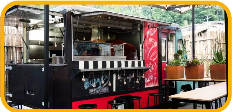 A stylish food truck with a seating area and decorative lights.
