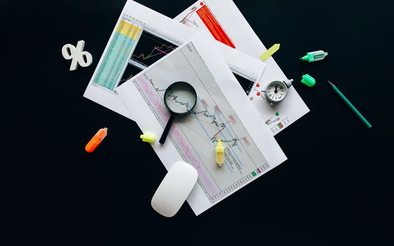 Printed financial statements, a magnifying glass and stationery laid out on a dark desk.