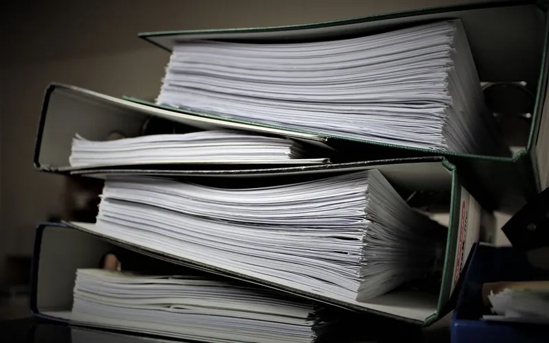 Overflowing binders of paper records waiting to be entered into the books.