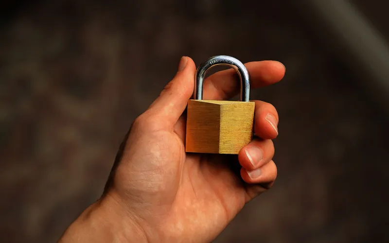 A hand holding a brass padlock, lit warm against a dark ground.