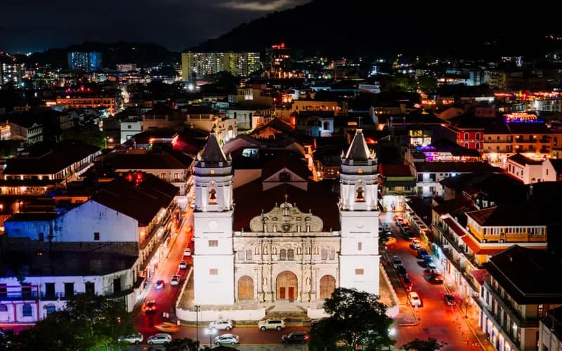 The Catedral Metropolitana lit among the tiled roofs of Casco Viejo at night.