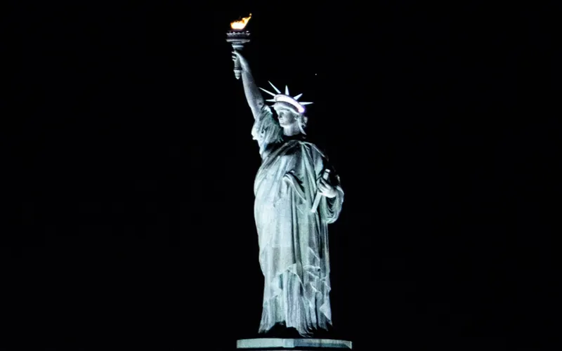 The Statue of Liberty floodlit against a black night sky, torch raised.