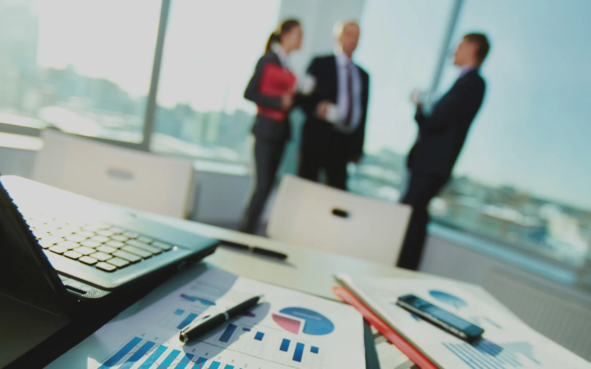 Printed charts and projections spread across a meeting-room desk beside a laptop.