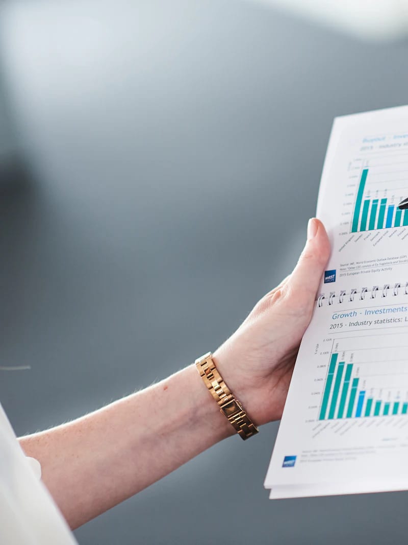 An auditor holding open a printed report of charts and figures.