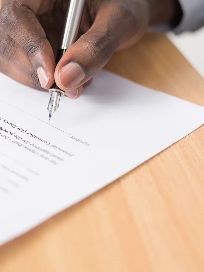 A hand signing a licence application form at an office desk.