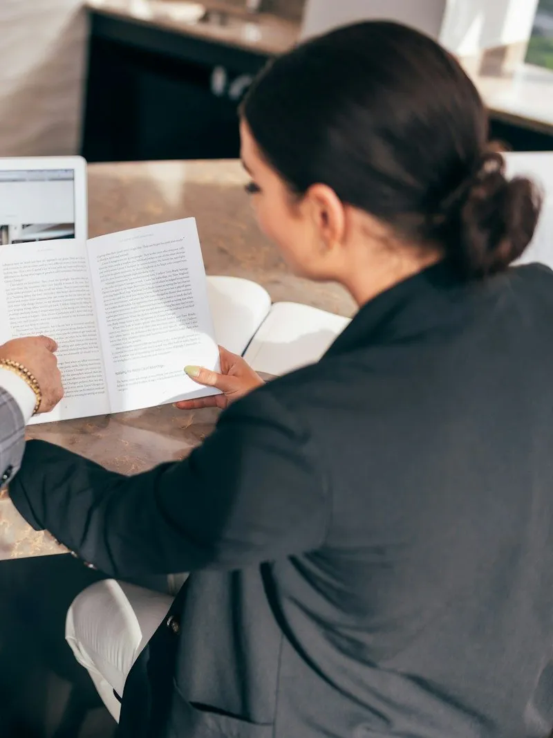 Two colleagues reading through an open printed document across a stone table.