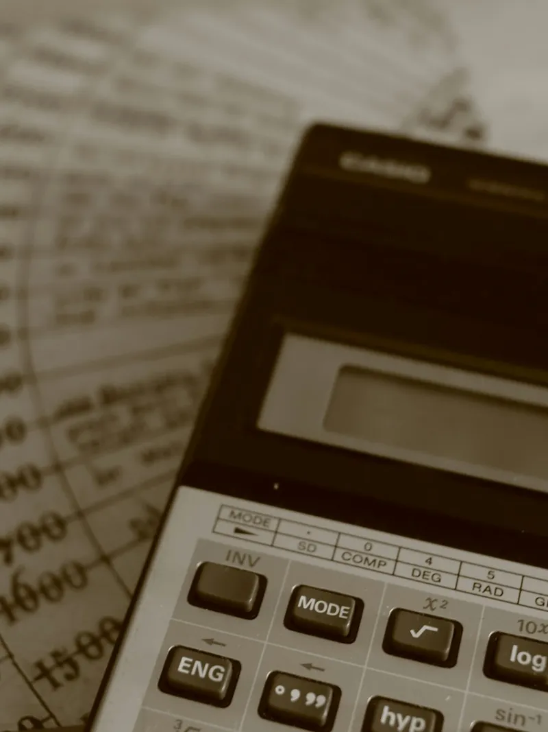 A calculator resting on printed ledger sheets of handwritten figures, lit warm.