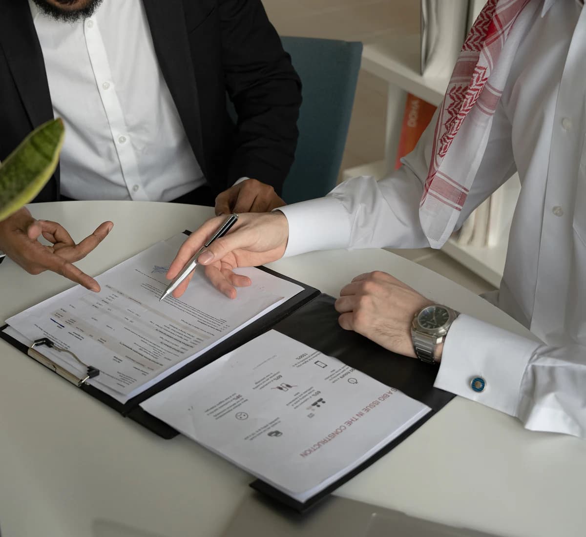 Two people going through licence paperwork together across a desk, one of them in a kandura.