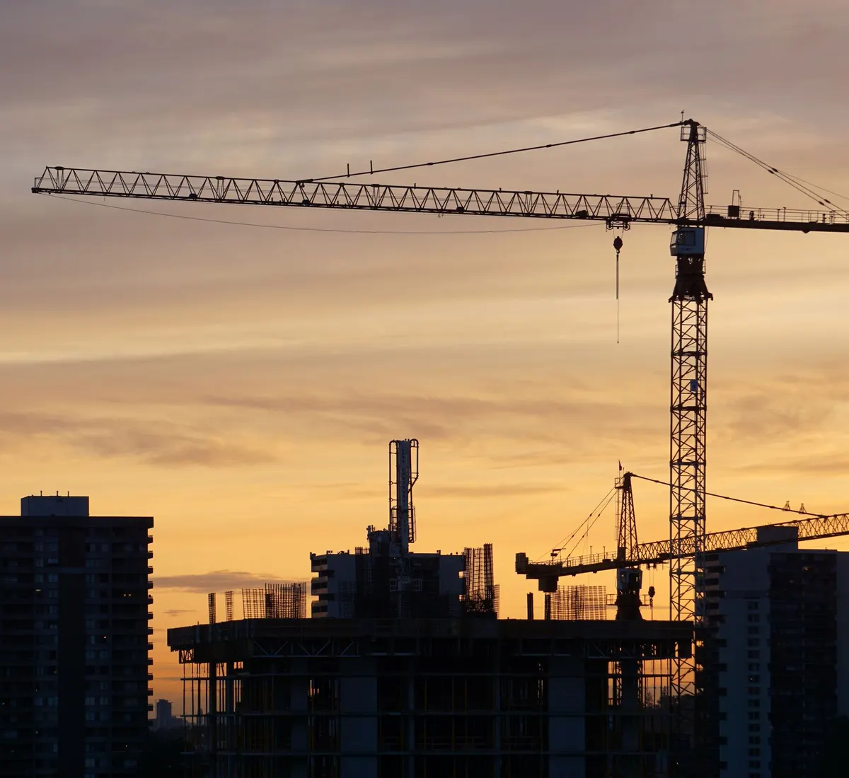 Tower cranes silhouetted over a building site against a sunset sky