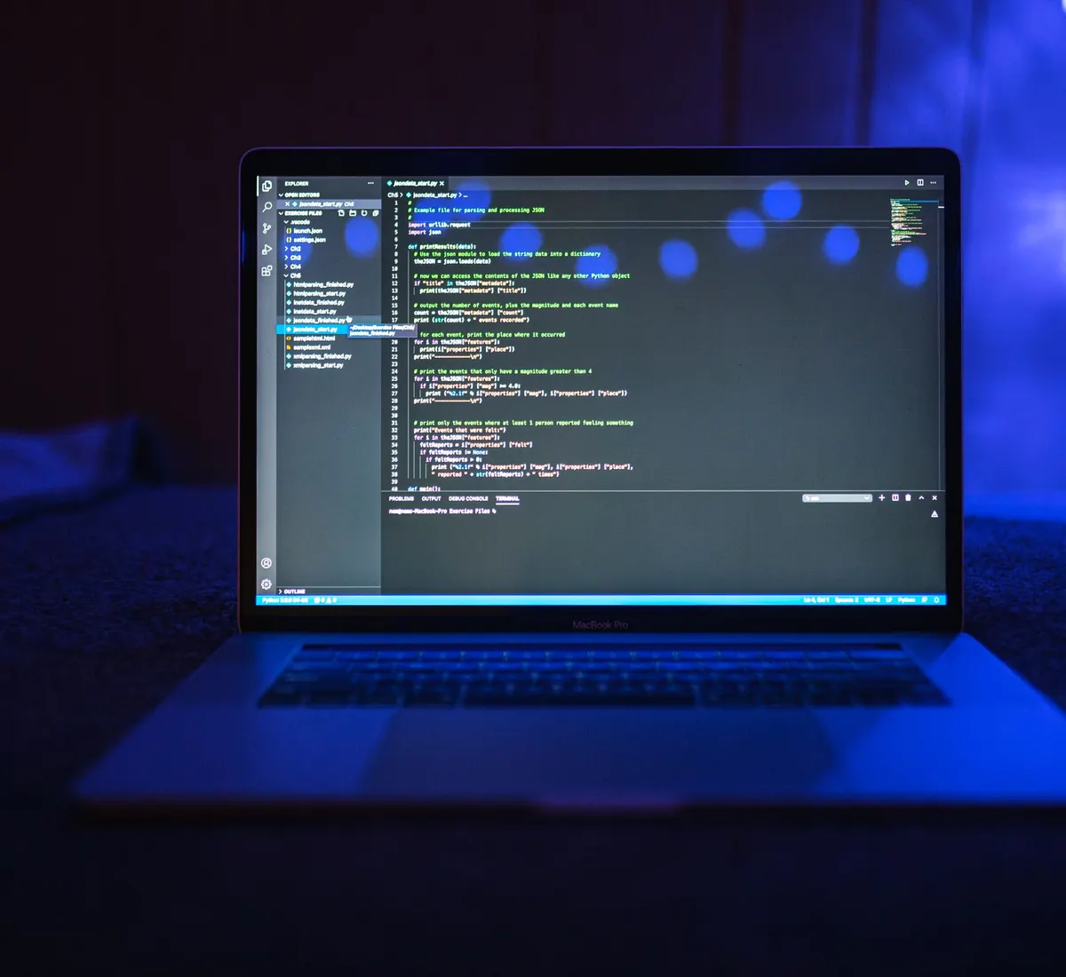 Laptop showing programming code in a dark room lit blue