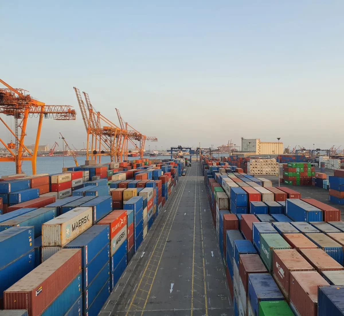 Stacked shipping containers and quay cranes along a container terminal at first light.