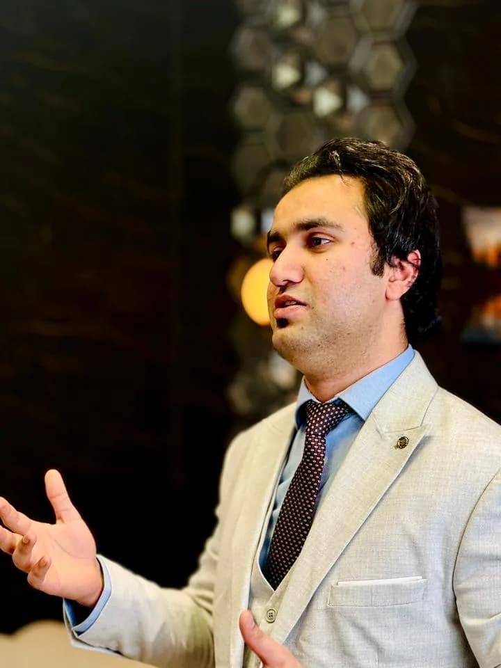 Haseeb Hamdani in a light suit, speaking and gesturing mid-sentence
