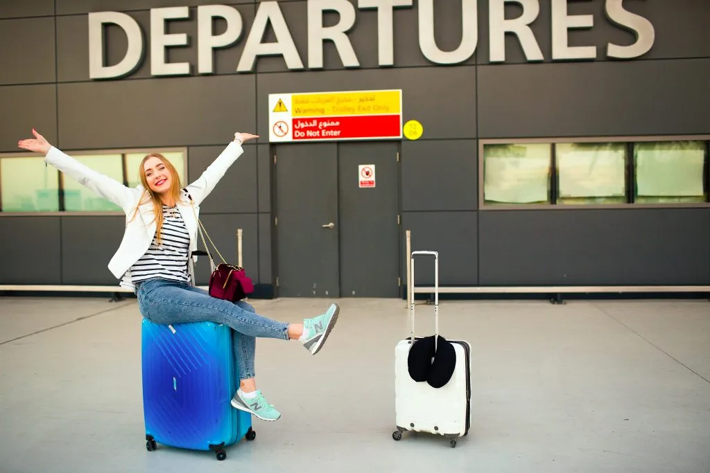 happy woman raises her hands up sitting blue suitcase before 1024x683 2